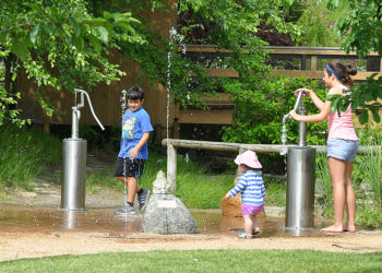three siblings playing outside at a public garden with water fountains
