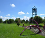 outdoors in early summer with a large blue campanile, a giant octapus sculpture and green grass and trees