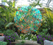sculpture made of reflective circles that shines in the light with the tropical plant conservatory and colorful flowers