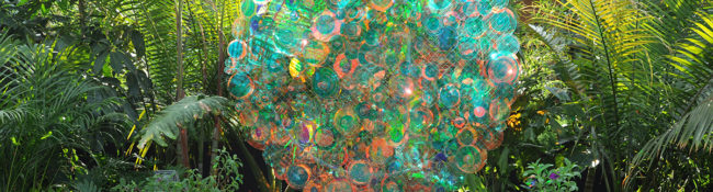 sculpture made of reflective circles that shines in the light with the tropical plant conservatory and colorful flowers