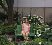 Reiman Gardens intern sitting on a bench and smiling while outside with whtie flwoers behind