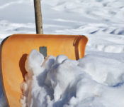 somebody holding a yellow show shovel and shoveling snow