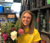 intern smiling while standing in the head house while holidng a bouquet of flowers with pink and white roses