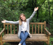 intern posing outside seated on a bench with their arms in the air