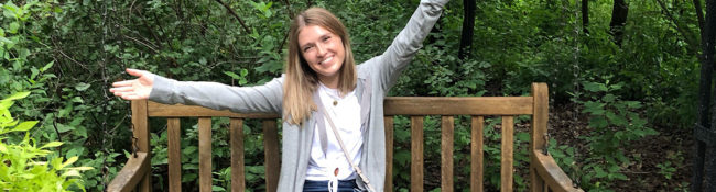 intern posing outside seated on a bench with their arms in the air
