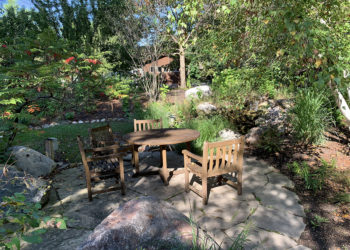 outdoors in the Natuarlist Garden in summer with trees, plants and a wood table and chairs