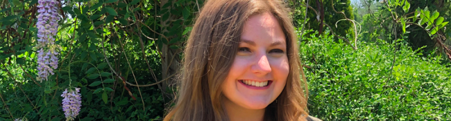 outdoors with a smiling Reiman Gardens intern with wisteria arbor behind