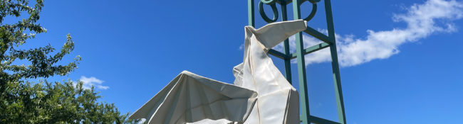 outdoors during spring with a large metal white origami sculpture and a campanile