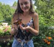 one of the interns outside during summer holding two monarch butterflies