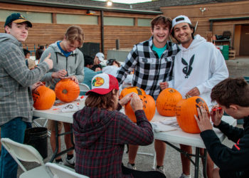 group of young adult volunteers smiling while carving pumpkins