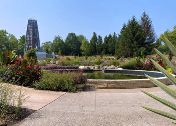 outdoors at a public garden with a lake, tower, trees and colorful plants